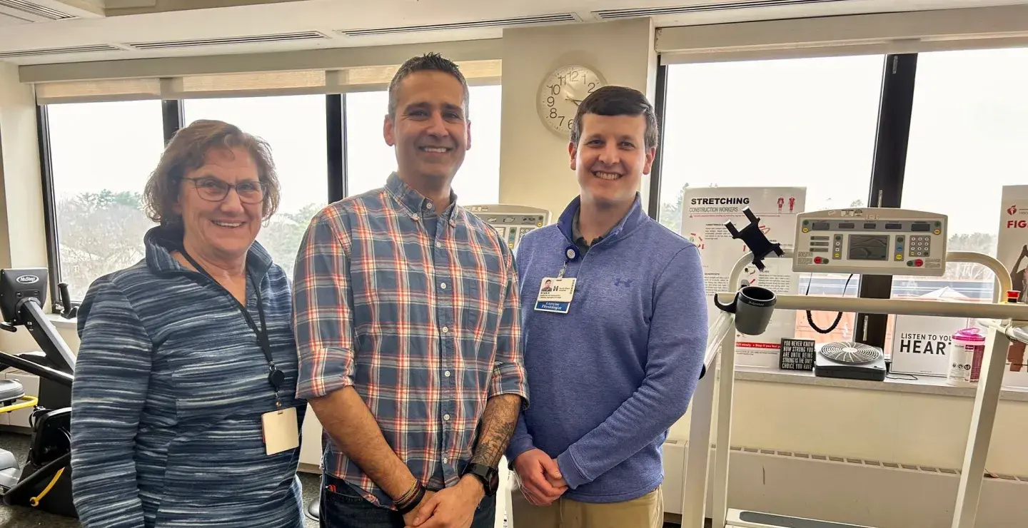 A male patient stands near a treadmill between a female nurse and male exercise physiologist