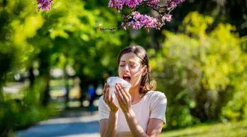 A woman with allergies about to sneeze standing beneath a blooming tree