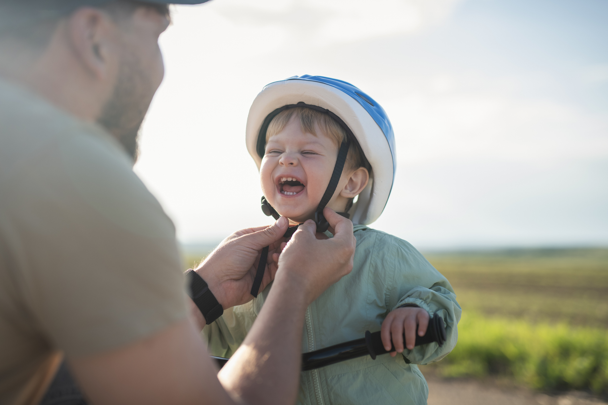 A little boy smiles as his dad adjusts his bike helmet before a bike ride.